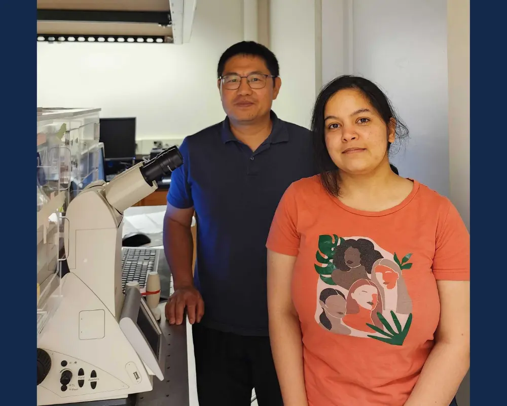 A man in a blue shirt and a woman in an orange shirt standing next to a microscope